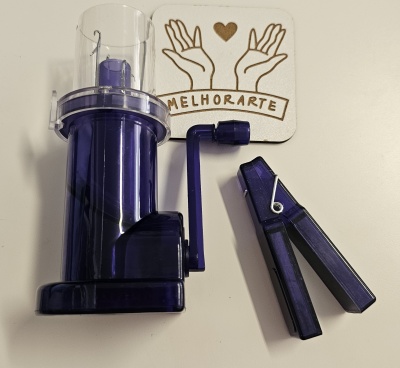 Máquina manual roxa com manivela ao lado e acessório em superfície branca com decoração MELHORARTE