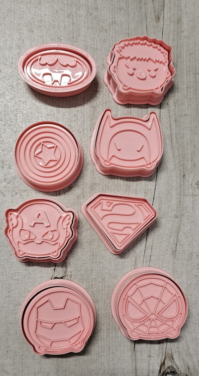 Cortadores de biscoito rosa com formas de super-heróis em madeira cinzenta