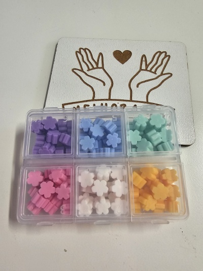 Seis caixas transparentes com peças coloridas em forma de flores em cima de um cartão branco com desenho de mãos e coração