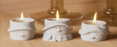 Três velas decorativas brancas acesas com suportes em forma de personagens sorridentes.