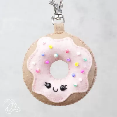 Porta-chaves em forma de donut cor de rosa com rosto sorridente e pompons coloridos