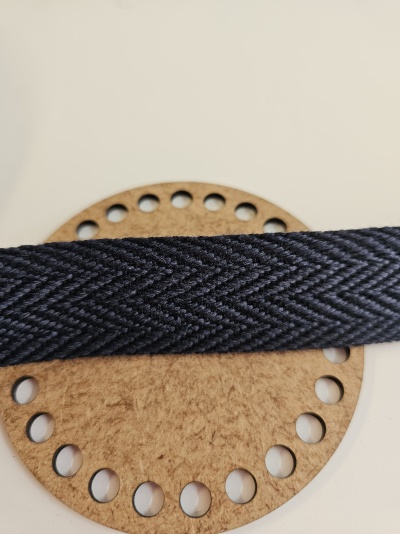 Fita têxtil preta espinha de peixe sobre círculo de cartão castanho com furos.