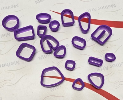 Moldes de corte para biscoitos em plástico roxo com várias formas geométricas sobre superfície branca com texto e linhas vermelhas