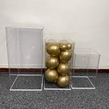 Três caixas acrílicas transparentes, uma com bolas douradas dentro.