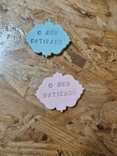Etiquetas azul claro e rosa com texto 'O MEU BATIZADO' em relevo sobre madeira clara.