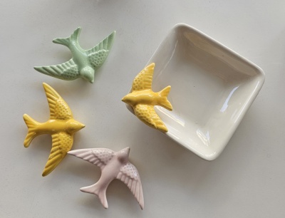 Passaros decorativos cerâmicos coloridos ao redor de prato branco quadrado