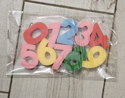 Números de espuma coloridos embalados em plástico sobre chão de madeira clara