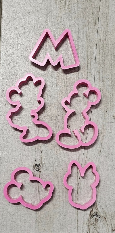 Cinco cortadores de bolachas rosa em várias formas sobre madeira clara.