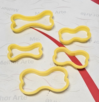 Conjunto de moldes amarelos em forma de osso sobre superfície branca e vermelha.