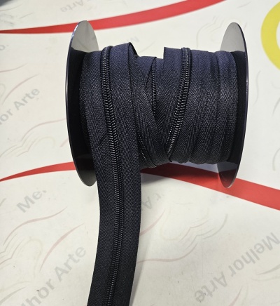 Rolo de fecho éclair preto numa bobina preta sobre superfície branca com texto e linhas coloridas