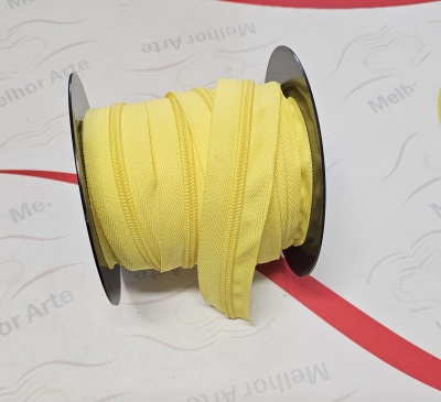 Fita ou viés amarelo enrolado num carretel preto numa superfície branca com texto 'Melhor Arte' e linha vermelha.