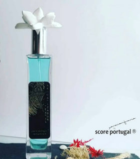 Frasco de perfume azul claro com flores brancas na tampa e etiqueta preta com padrão dourado