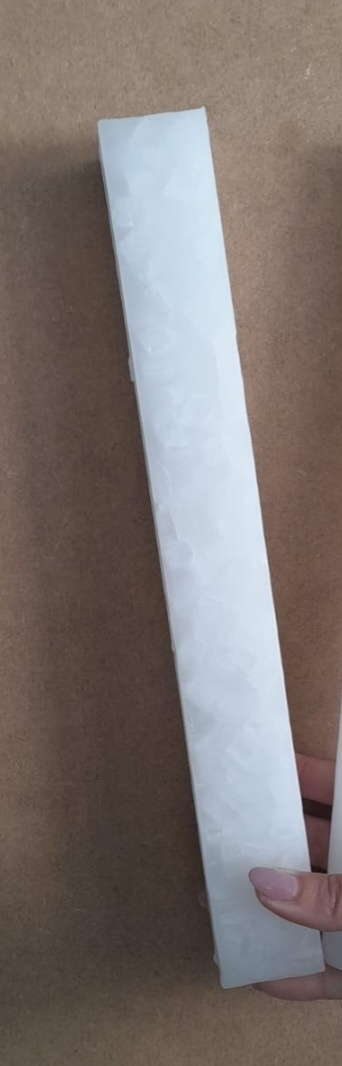 tira branca longa com textura cristalina segurada por uma mão sobre fundo castanho