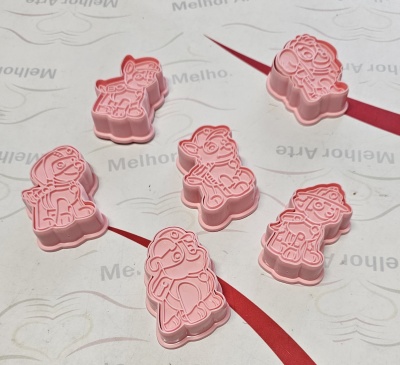 Moldes cor-de-rosa para biscoitos com formas de personagens animados sobre superfície branca com texto 'Melhor'