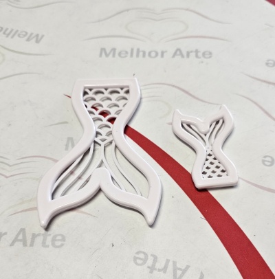 Duas cortantes de plástico branco em forma de cauda de peixe com padrões vazados, sobre superfície branca com texto.