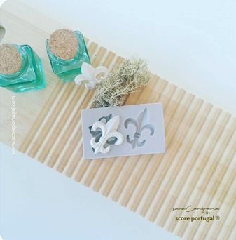 Garrafinhas de vidro verde, molde de silicone cinza e flor-de-lis branca sobre madeira clara com ranhuras