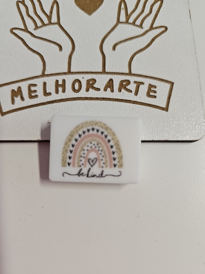 Produto quadrado branco com desenho de arco-íris e texto 'be kind' sobre cartão com ilustração de mãos e texto 'MELHORARTE'.