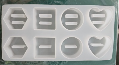 Forma de silicone branca com cavidades em formatos variados, incluindo hexágono, retângulo, círculo e coração.