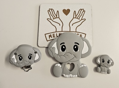 Brinquedos de silicone cinzentos em forma de elefantes com olhos grandes sobre fundo branco com cartão decorativo.