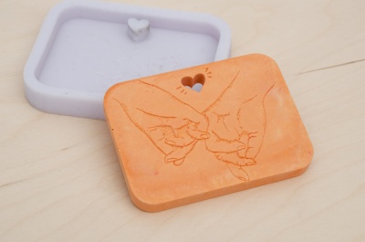 Molde de silicone lilás e sabonete cor de laranja com desenho de mãos unidas.