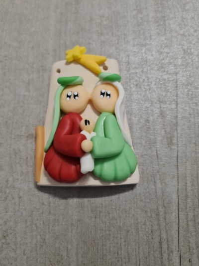 Figura decorativa de duas personagens em roupas vermelha e verde com bebé e estrela amarela no topo