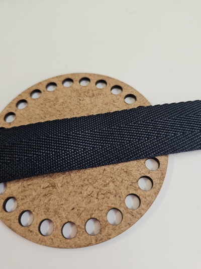 Círculo de cortiça com furos e fita preta texturizada deitada em cima, fundo branco.