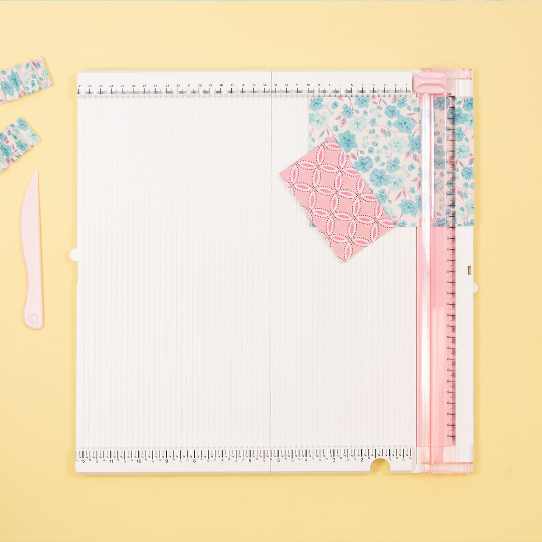 Prancha de corte branca com régua rosa e papéis decorativos coloridos