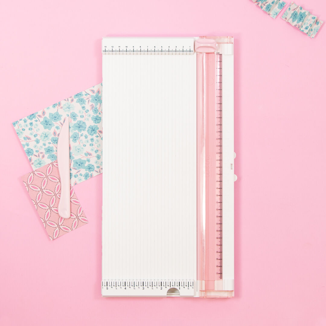 Máquina recortadora branca e rosa com papéis decorativos e ferramenta de corte