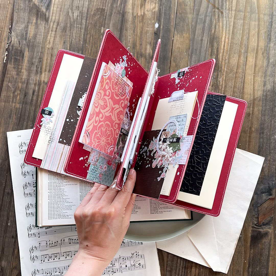 Reserva Workshop Presencial | Olena Khyzníak | Mel's Scrap Álbum vermelho decorado aberto sobre mesa com folhas de música e carta