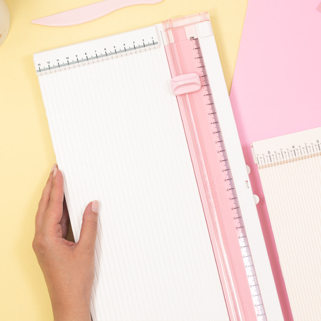 Três cortadores de papel com régua integrada e uma mão humana segurando um deles