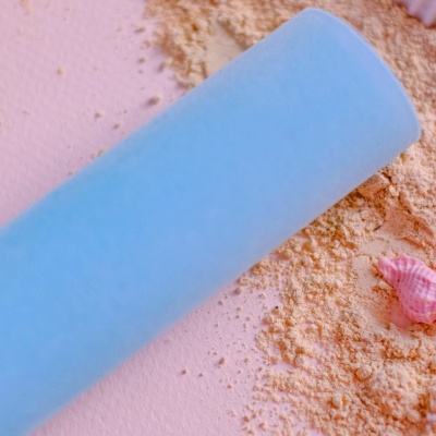 Rolo de massagem azul claro com pó amarelo e conchas decorativas sobre fundo rosa.
