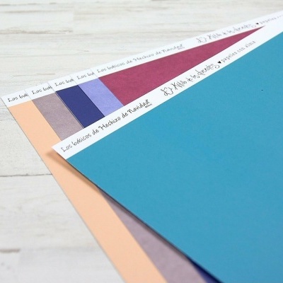 Folhas coloridas com texto manuscrito na faixa branca no topo sobre superfície clara.