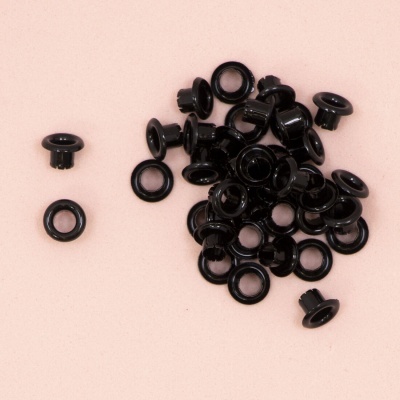 Conjunto de ilhós ou rebites pretos redondos numa superfície rosa