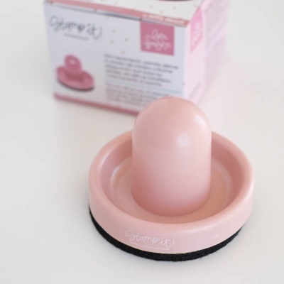 Carimbo redondo rosa com base preta e caixa rosa ao fundo