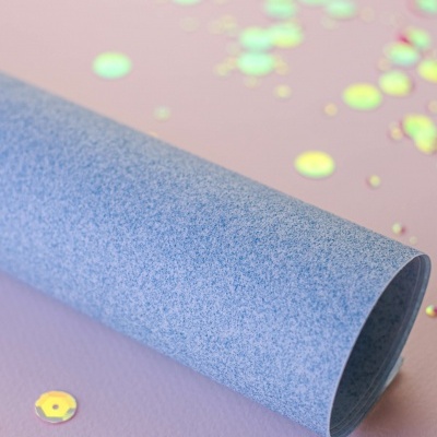 Rolo azul de papel texturizado sobre superfície lilás com lantejoulas brilhantes