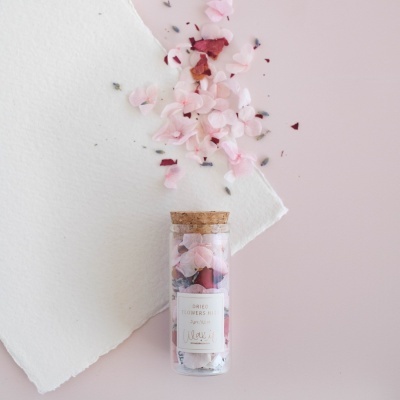 Frasco de vidro com pétalas de flores secas e tampa de cortiça sobre superfície rosa