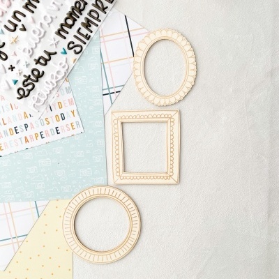 materiais para scrapbook com letras adesivas, papéis coloridos, molduras de madeira pequenas e recipiente com elementos artísticos