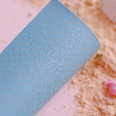 Tapete azul claro com bolinhas brancas sobre superfície rosa com areia e conchas