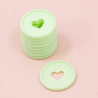 Discos circulares verdes claros com recorte de coração sobre superfície rosa