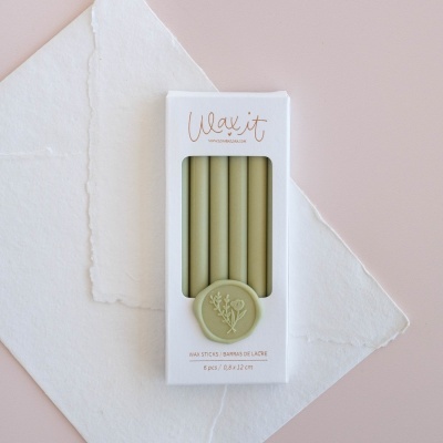 Caixa branca com cinco velas verdes e selo decorativo, texto Wax it, sobre papel branco e fundo rosa