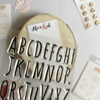 Carimbos de letras do alfabeto transparentes sobre base de madeira com decoração floral e botões