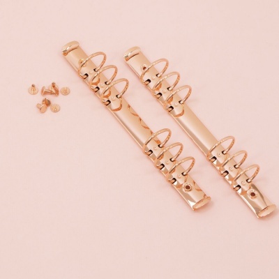 Conjunto de presilhas douradas com molas e parafusos num fundo rosa