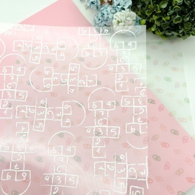 Folha de papel transparente com padrão branco de jogo da amarelinha, sobre folhas rosa e branca com padrões suaves
