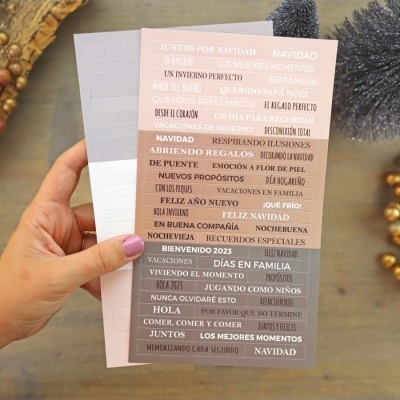 Autocolantes temáticos de Natal e Ano Novo em tons pastel segurados por uma mão, fundo de madeira.