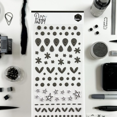 Cartão de autocolantes Puffy pretos com vários desenhos e materiais de arte em preto e branco ao redor.