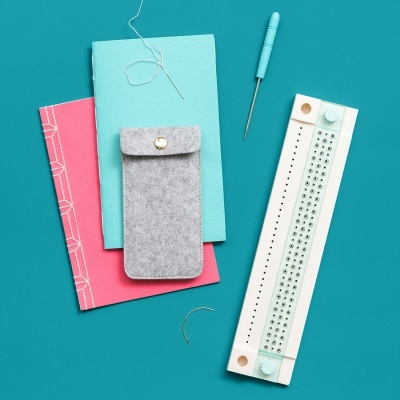 Kit para tricô com malha, agulhas, agulha de costura, bolsa de feltro e cadernos sobre fundo azul