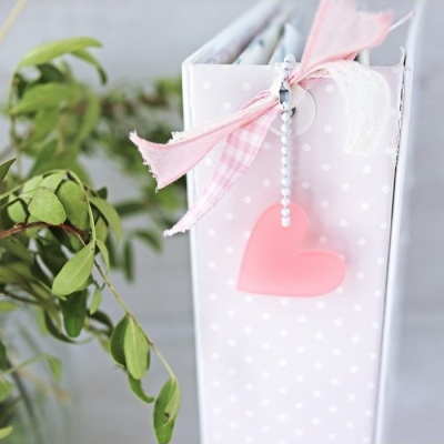 Caderno branco com pontos e decoração com fitas e coração cor-de-rosa.