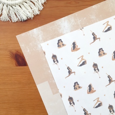 Papel decorativo com ilustrações de mulheres em posições de ioga sobre mesa de madeira clara