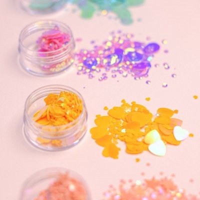 Quatro frascos com purpurinas coloridas em superfície rosa