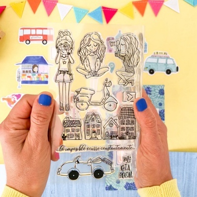 Conjunto de carimbos transparentes com desenhos e textos, mãos segurando, fundo decorado colorido.